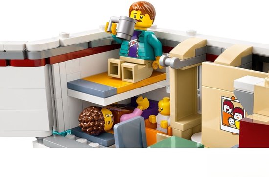 LEGO minifiguur in een camper met bed en mok. Een babyfiguur zit op de vloer.