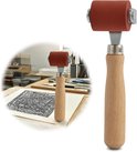 Een rode rol met houten handvat, met op de achtergrond een werkplaats en een print.