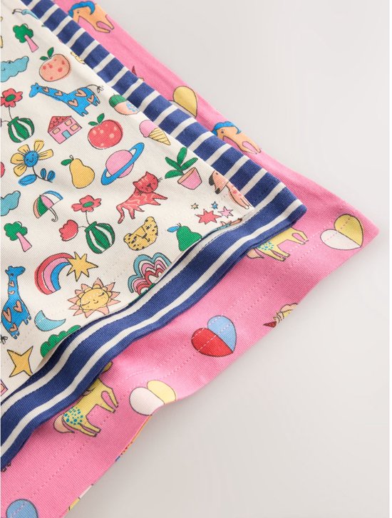 Close-up van drie opgestapelde hemdjes met diverse prints: wit met iconen, blauw-wit gestreept en roze met eenhoorns.