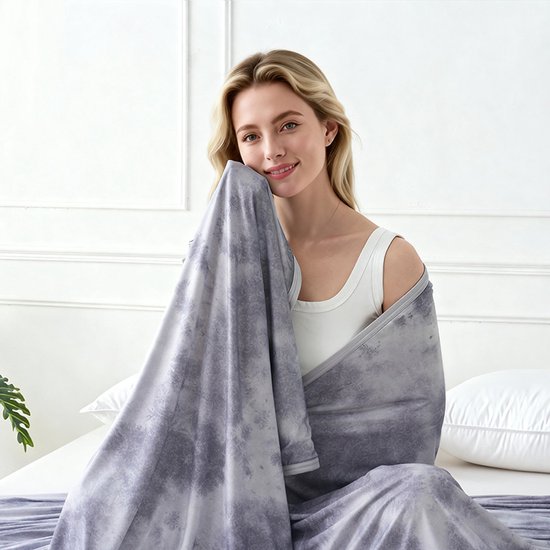 Vrouw met grijze tie-dye deken om zich heen, zittend op een bed.