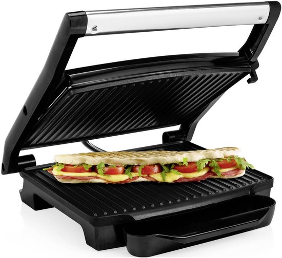 Open zwarte grill met een lange panini in, gevuld met brood, kaas, tomaat en sla. Een halve panini op een bord ernaast.