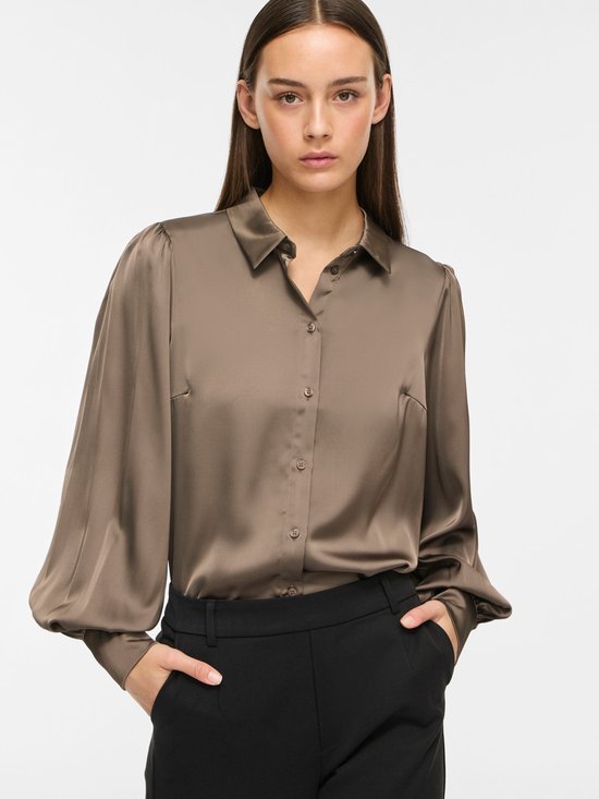 Model in taupe satijnen blouse met pofmouwen en zwarte broek.