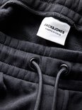 Close-up van de tailleband van een zwarte sweatbroek met trekkoord en label JACK&JONES PANTS STUDIO.