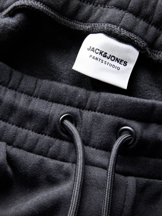 Close-up van de tailleband van een zwarte sweatbroek met trekkoord en label JACK&JONES PANTS STUDIO.