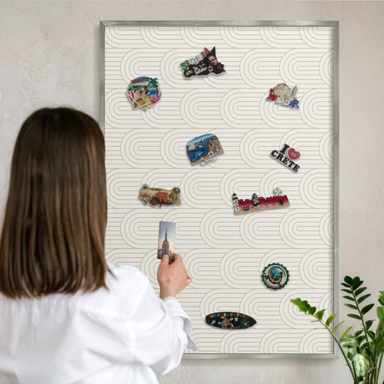 Vrouw met bruin haar hangt een magneet op een magneetbord met geometrische beige bogen.