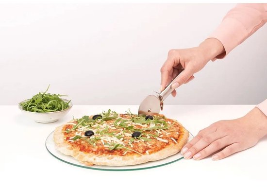 Main coupant une pizza avec de la roquette et des olives noires à l'aide d'un coupe-pizza en acier inoxydable.