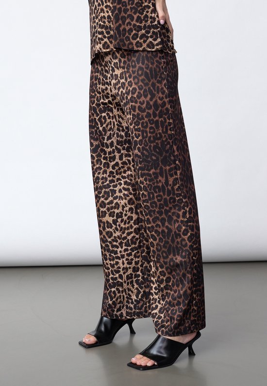 Model in wijdvallende broek met luipaardprint en zwarte sandalen.