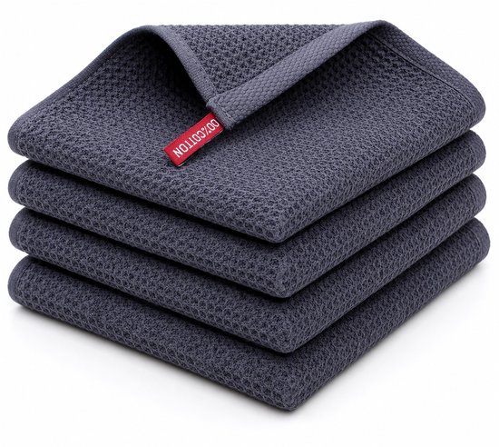 Pile de quatre torchons gris foncé à texture gaufrée, avec une étiquette rouge '100% COTTON'.