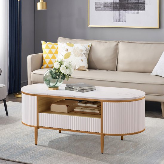 Ovale salontafel met marmerlook blad, wit geribbeld design en gouden poten. Met open vakken en boeken.