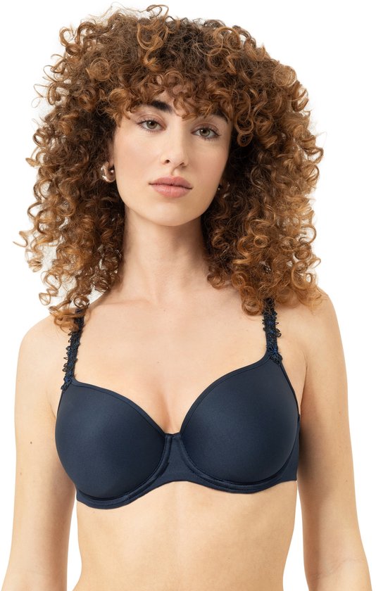 Model met krullend bruin haar draagt een marineblauwe beugelbeha met decoratieve, geborduurde bandjes.