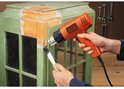 Persoon gebruikt een oranje BLACK+DECKER heteluchtpistool om verf van een groene kast te verwijderen.