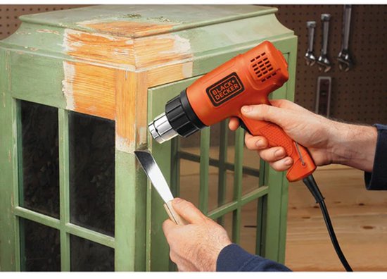 Persoon gebruikt een oranje BLACK+DECKER heteluchtpistool om verf van een groene kast te verwijderen.