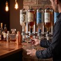 Man schenkt drank uit flessen met etiketten 'Old Oak Gin', 'Highland Reserve Whisky' en 'Sol Azul Tequila'.