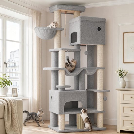 Grijze kattenkrabpaal met meerdere verdiepingen, hangmatten en holletjes, in een woonkamer. Katten spelen op de paal, terwijl een vrouw ernaast staat.