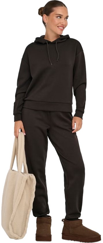 Een model met haar in een knot, draagt een donkerbruine hoodie en joggingbroek, met een beige teddy shopper en bruine laarsjes.