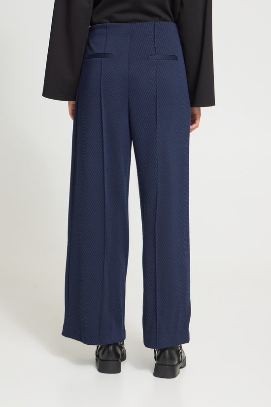 Aanzicht op de achterkant van een model met een donkerblauwe broek met wijde pijpen.