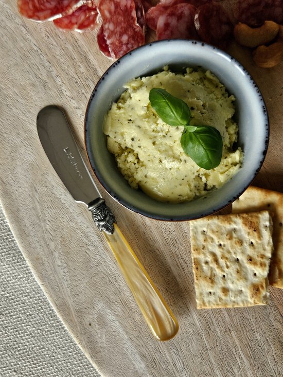 Boter mes met een crème-kleurig handvat en zilverkleurig heft, naast een kom met boter, crackers en vleeswaren.