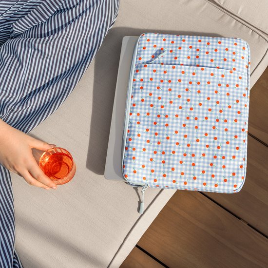 Persoon met gestreepte blouse houdt een glas vast naast een laptop sleeve met kersenprint.