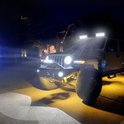 Een donkergekleurde Jeep Wrangler staat 's nachts op een oprit, verlicht door krachtige LED-lampen op de bumper en het dakrek.