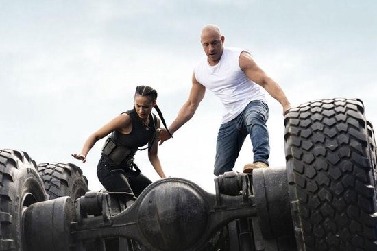 Vin Diesel en Michelle Rodriguez klimmen op een omgedraaide truck met grote banden.