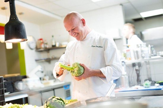Chef met witte jas snijdt artisjokken in een keuken.