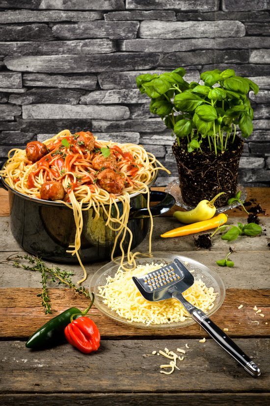 Spaghetti met gehaktballetjes in tomatensaus, geserveerd met geraspte kaas, pepers en basilicum.