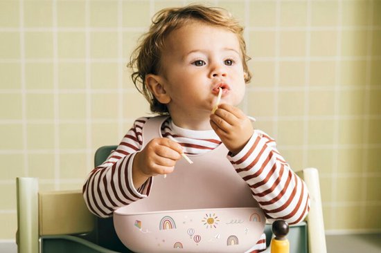 Een baby met rood-wit gestreept shirt en roze slab eet spaghetti in een kinderstoel.