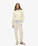 Model in een off-white, halve rits trui met kraag, gedragen over een lichtblauw gestreept overhemd, met bijpassende joggingbroek.