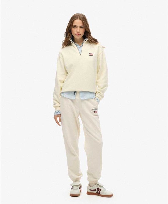 Model in een off-white, halve rits trui met kraag, gedragen over een lichtblauw gestreept overhemd, met bijpassende joggingbroek.