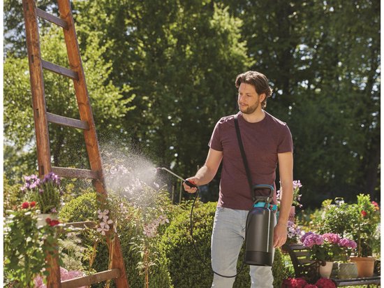 Man met donkergrijze GARDENA drukspuit met blauwe details op de schouder, sproeit planten met een lange lans.