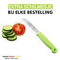 Éplucheur vert avec une lame, à côté d'une tomate et de rondelles de concombre.