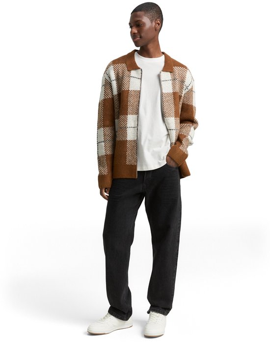 Man met bruin en wit geruite vest, zwarte jeans en witte sneakers.