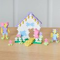 Pastel Plus-Plus bouwset met een huisje, twee figuurtjes en bloemen in paars, geel, wit, groen en blauw.