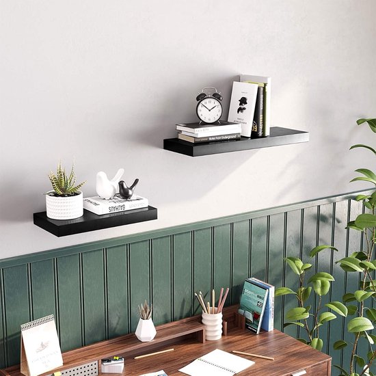 Zwarte zwevende planken op een muur boven een bureau, met decoraties.