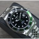 Automatisch herenhorloge met zwarte wijzerplaat, groene lunette en zilverkleurige band op standaard.