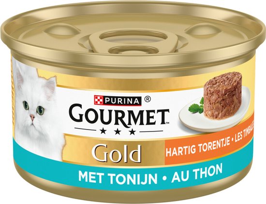 Blikje Gourmet Gold Hartig Torentje met Tonijn kattenvoer. Een witte kat kijkt naar de camera, naast een portie van het voer op een schoteltje.