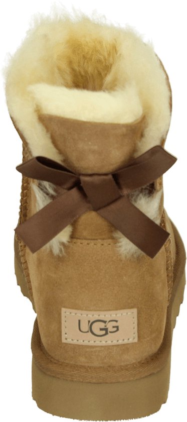 Achterkant van cognackleurige enkellaarsjes van suède met witte schapenwollen voering, strikdetail en UGG-logo.
