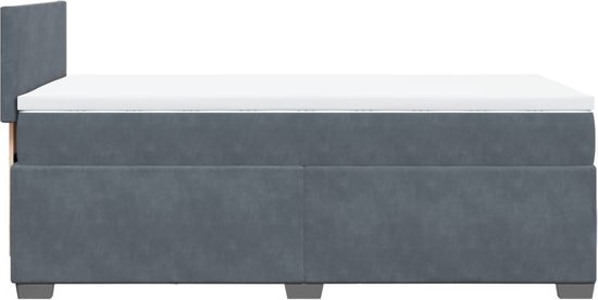 Vue latérale d'un lit tapissé gris foncé avec matelas et tête de lit, sur pieds noirs.