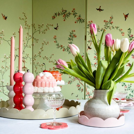 Rode en roze peper- en zoutmolens op een dienblad, naast roze tulpen in een vaas.