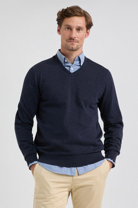 Man draagt een marineblauwe V-hals trui over een lichtblauw overhemd, met een beige broek.