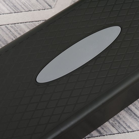 Close-up van het geribbelde, antislip oppervlak van een zwarte aerobic step met een grijs ovaal element.