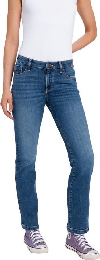 Vrouw in een bootcut spijkerbroek in medium blauw denim, met witte top en paarse sneakers.