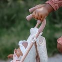 Een kind duwt een roze poppenbuggy met een pop erin, die een roze jasje en witte kleding draagt.