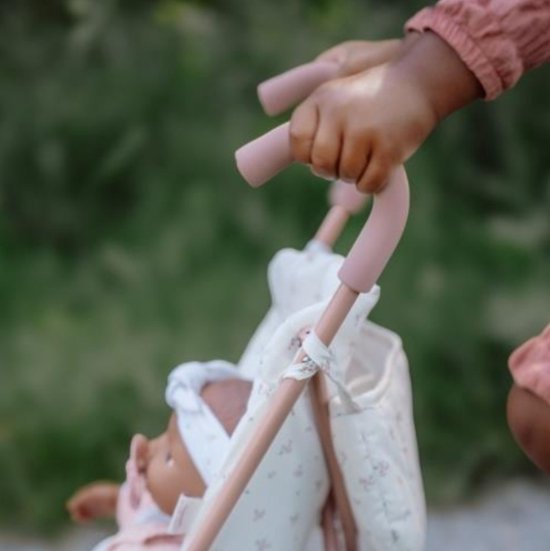 Een kind duwt een roze poppenbuggy met een pop erin, die een roze jasje en witte kleding draagt.