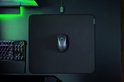 Zwarte Razer DeathAdder V3 hyperspeed gaming muis op een zwarte muismat, naast een mechanisch toetsenbord met groene verlichting.