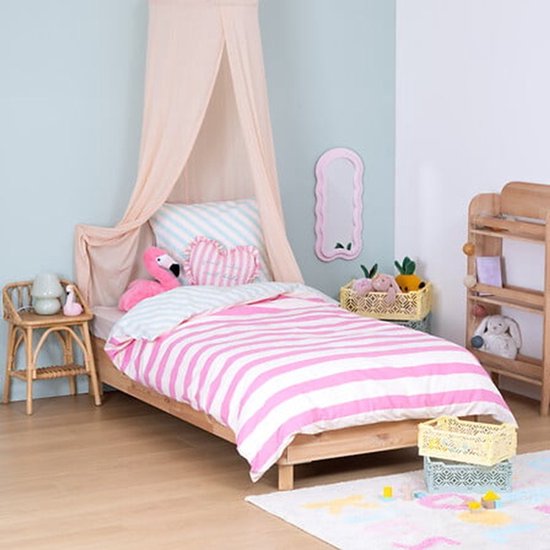 Miroir rose ondulé sur un mur bleu clair au-dessus d'un lit à rayures rose et blanc.