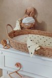 Rotan aankleedmand met baby spullen, met gele hydrofiele doekjes met zwarte hartjes.