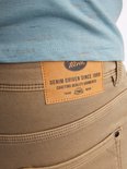 Close-up van het leren Petrol Industries 'Denim Driven Since 1989' label op een bruine chino.