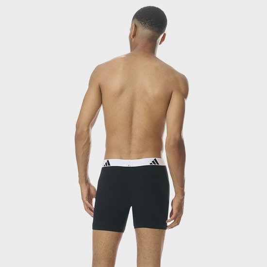 Model van achteren gezien, draagt een zwarte boxershort met witte adidas tailleband.