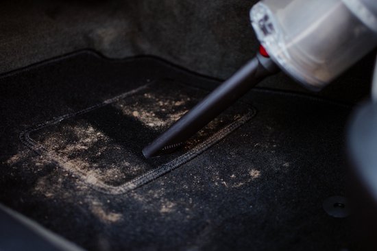 Tapis de voiture noir nettoyé sur un sol poussiéreux dans une voiture.